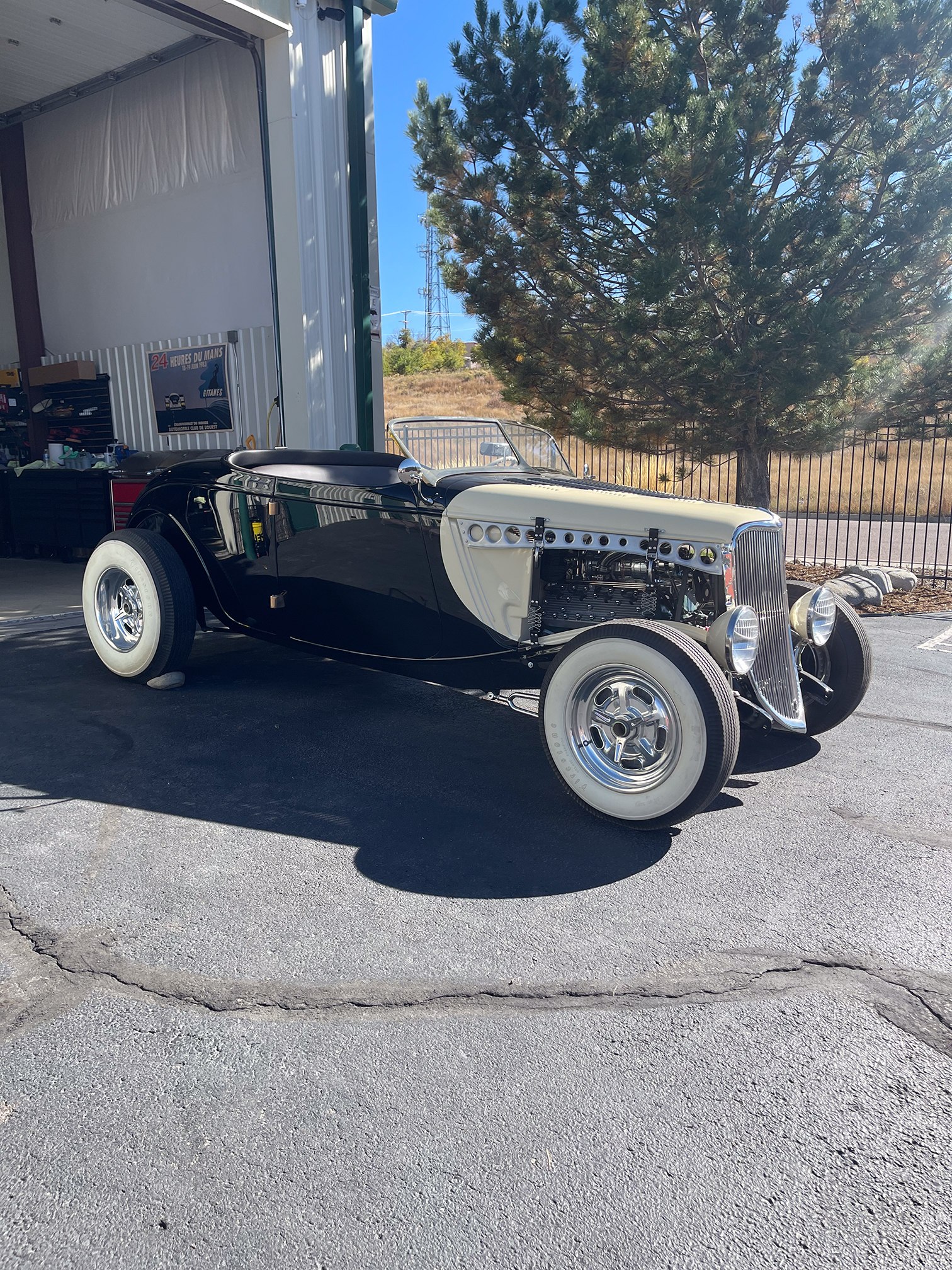 Black open-top classic roadster with cream wheels outside the workshop Black open-top classic roadster with cream wheels outside the workshop