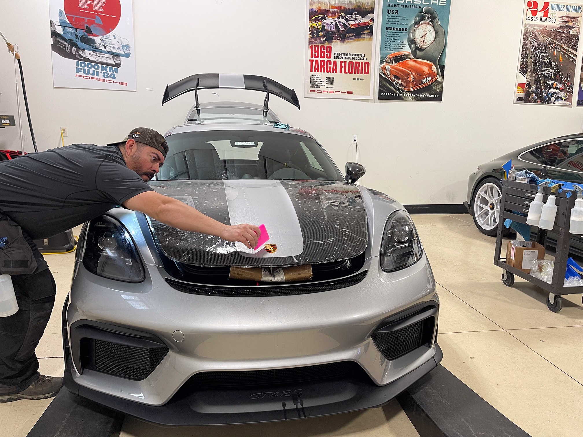 Installer using a pink squeegee on wet film over a silver Porsche Cayman hood Installer using a pink squeegee on wet film over a silver Porsche Cayman hood