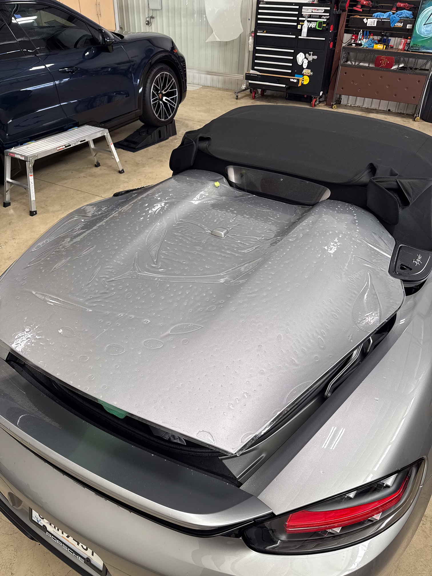 Wet clear film laid over the rear deck of a silver Porsche convertible Wet clear film laid over the rear deck of a silver Porsche convertible