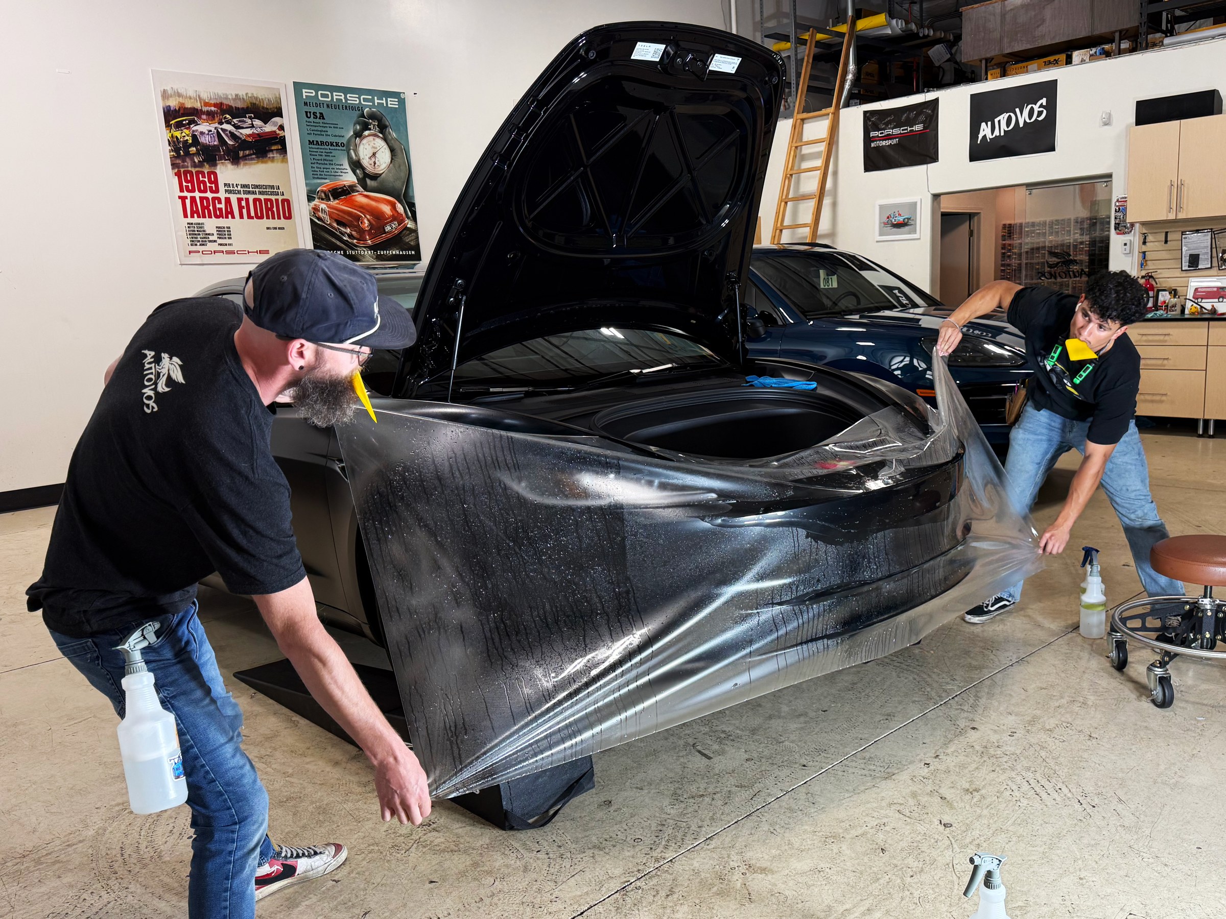Two installers positioning clear paint protection film around a car’s front bumper