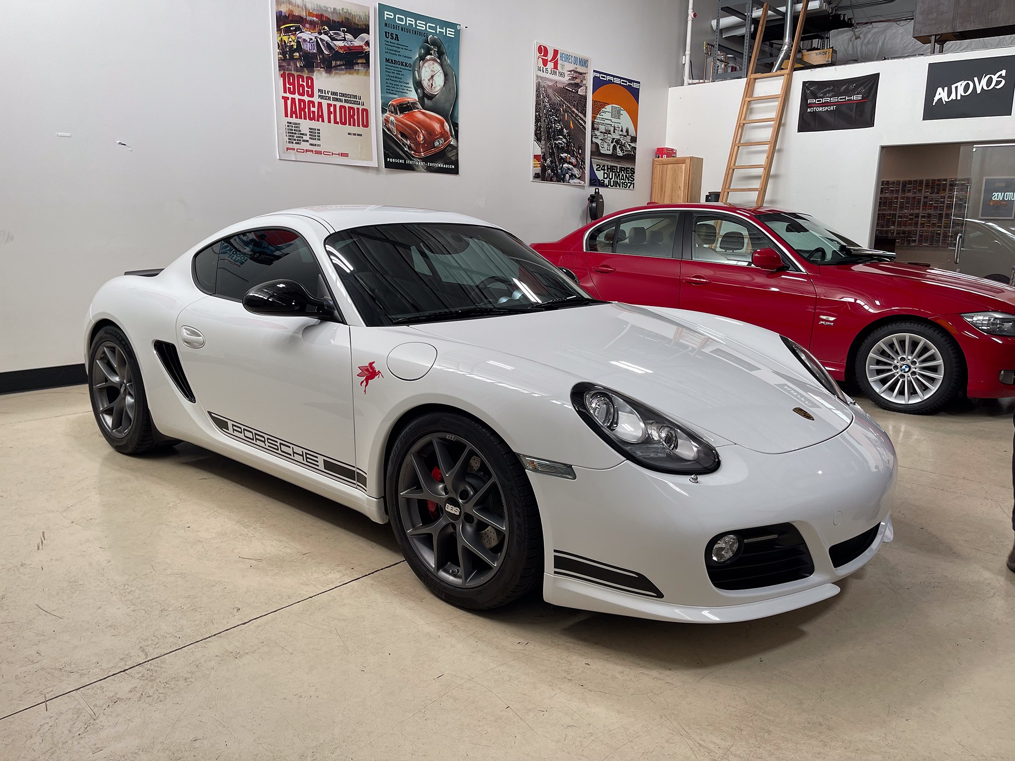 White Porsche Cayman with black wheels and side graphics in the workshop White Porsche Cayman with black wheels and side graphics in the workshop