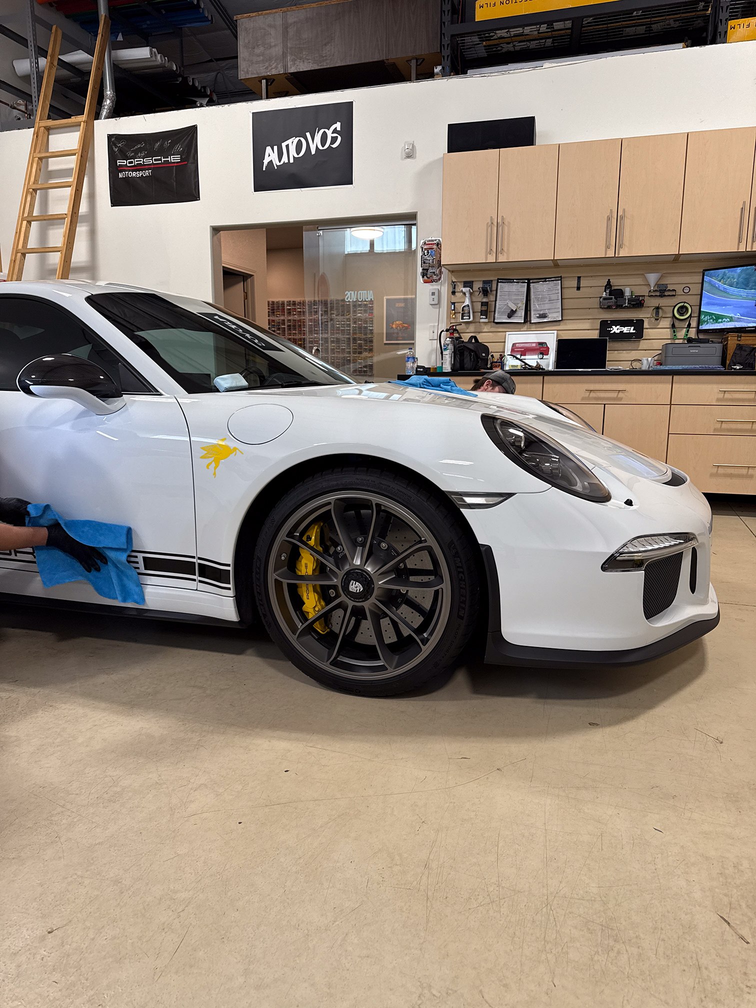 Gloved hand wiping the lower door of a white Porsche beside its front wheel Gloved hand wiping the lower door of a white Porsche beside its front wheel