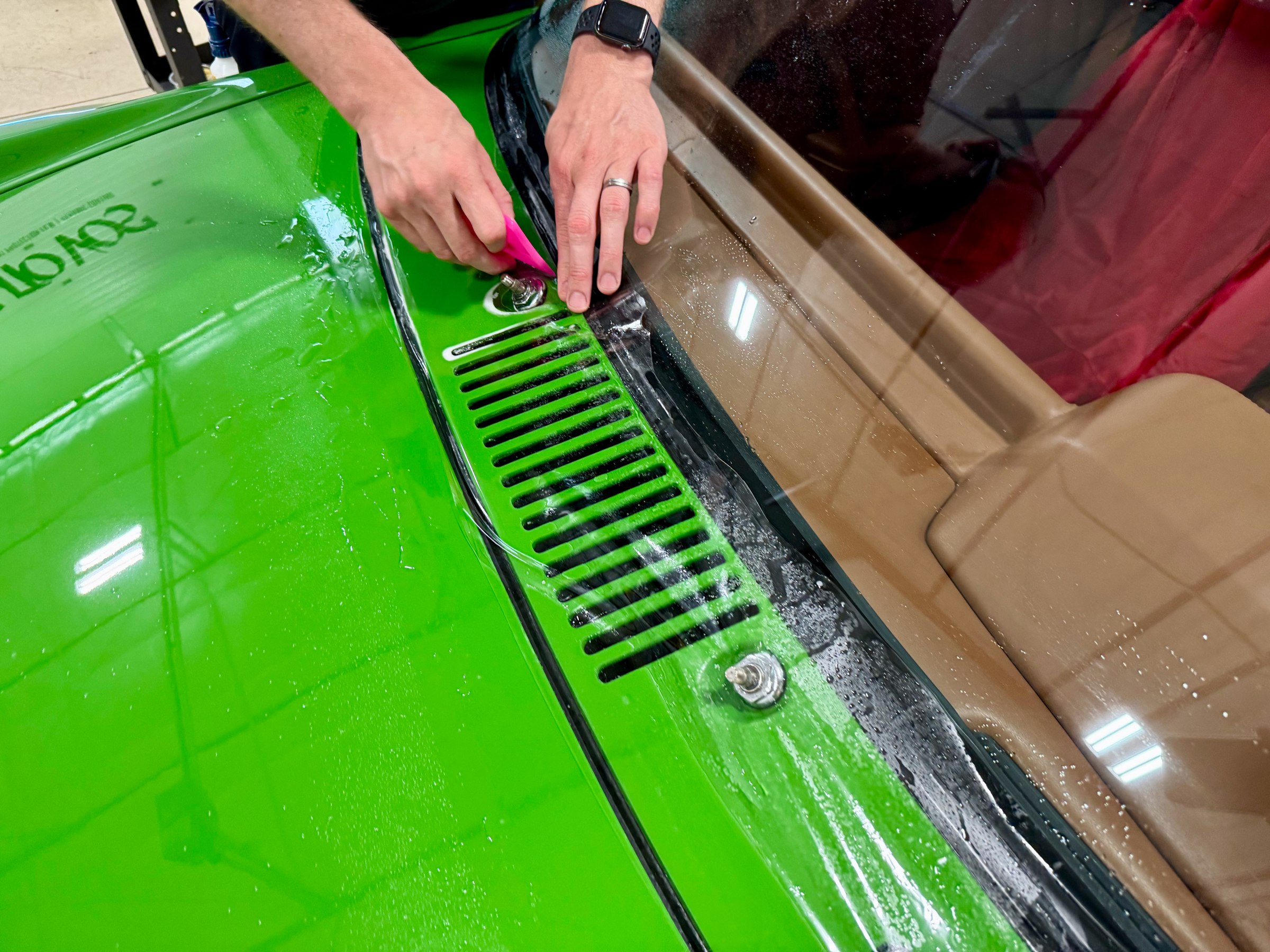 Squeegee working windshield protection film along the lower glass of a green Porsche 914 Squeegee working windshield protection film along the lower glass of a green Porsche 914