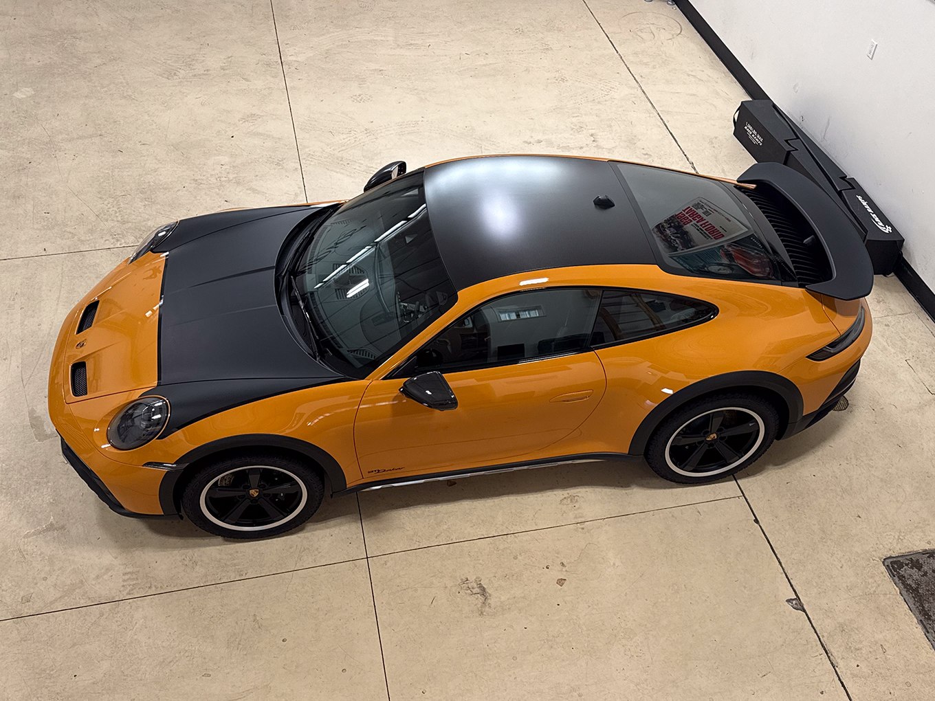 Overhead view of an orange Porsche 911 with a black hood, roof and rear wing at Auto Vos